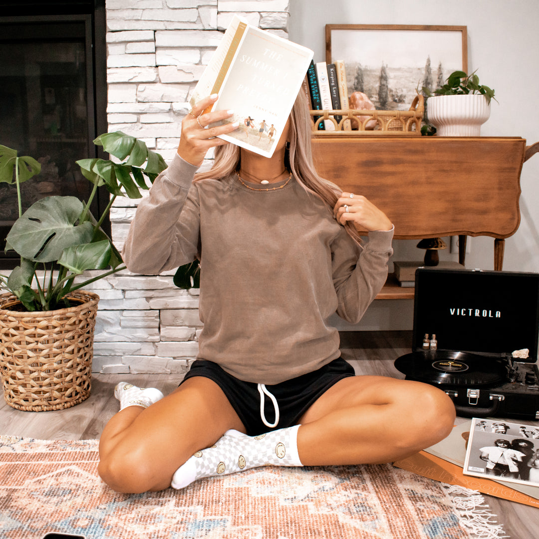 a woman wearing a brown long sleeve t-shirt while holding a book and sitting in a cozy living room