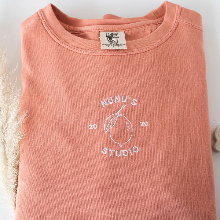 a salmon colored sweatshirt with a white logo embroidered on it.