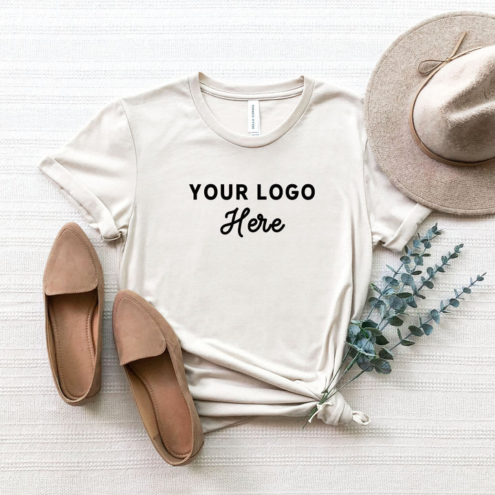 a light grey t-shirt with a custom logo on a cream background staged with plants